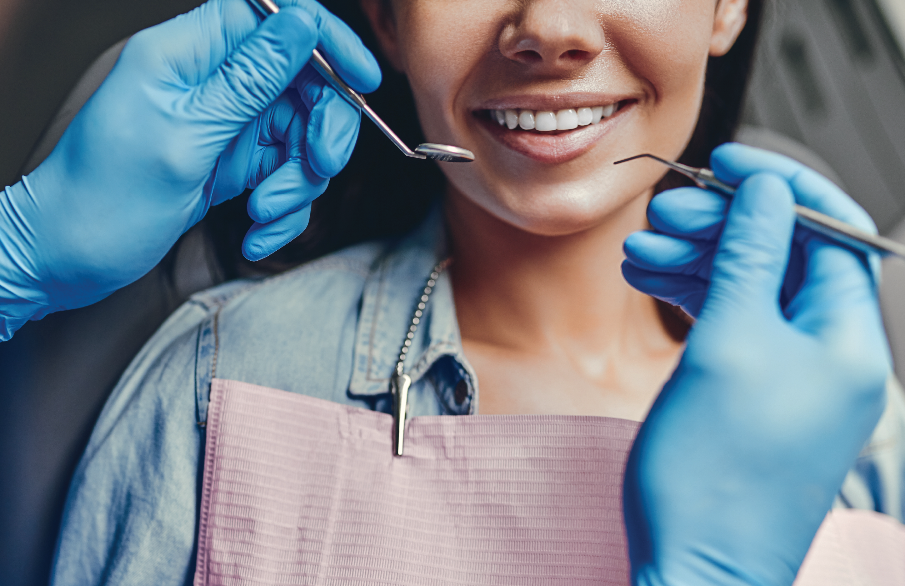 Person smiling in chair with dentist holding tools near their teeth