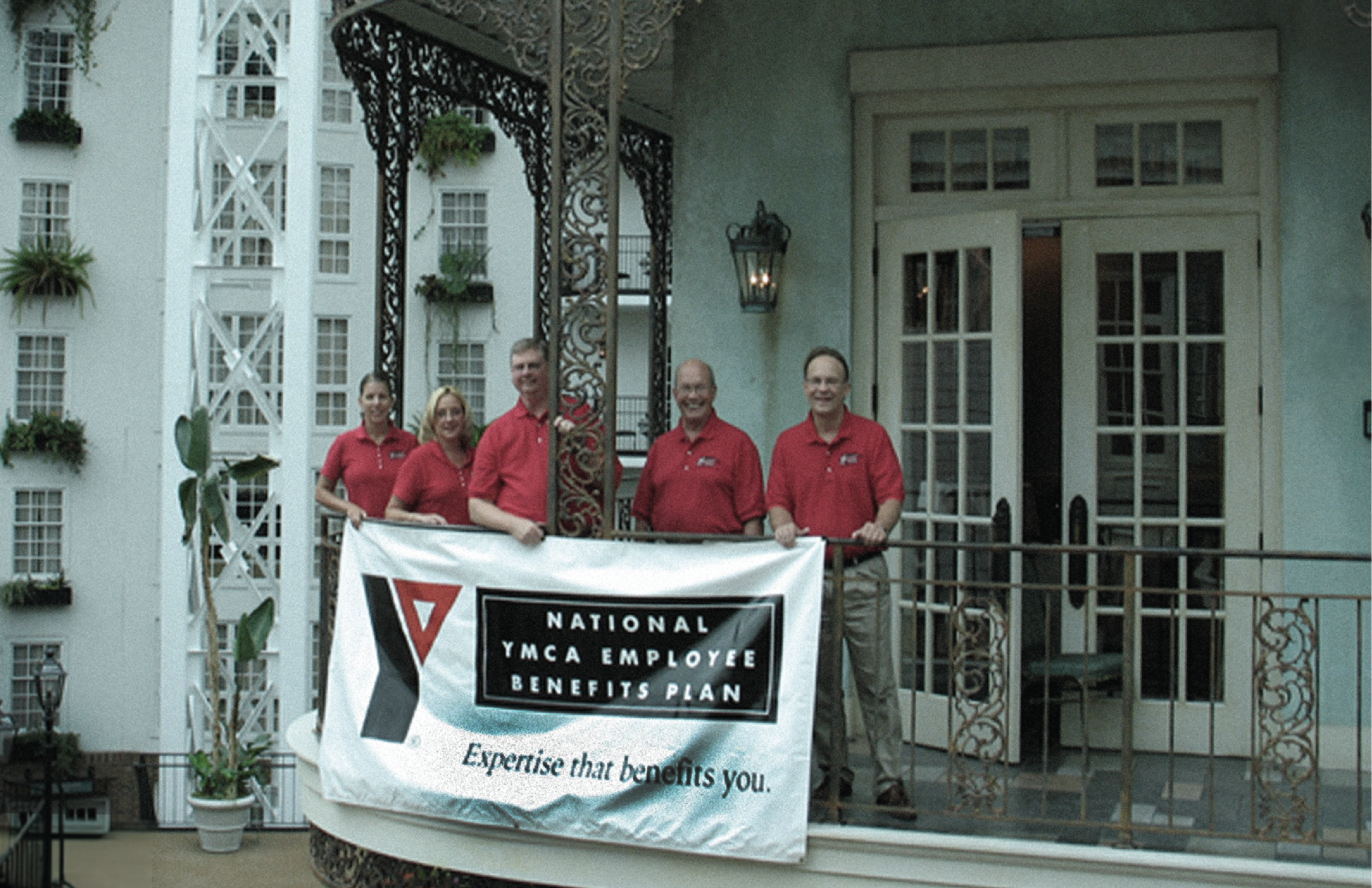 YMCA Employee Benefits team members pose on a balcony with a banner that reads "National YMCA Employee Benefits Plan, Expertise that benefits you."